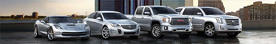A silver sports car, sedan, ute and SUV are lined up on a building rooftop, with a city skyline in the background.