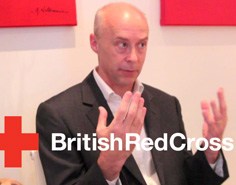 A man in a suit holds up both hands, with the text "British Red Cross" and the company's logo superimposed.