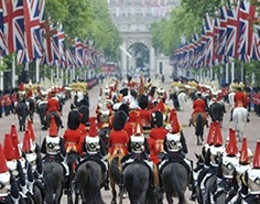 A wide shot of The Royal Guard on horseback, marching down a road lined with British flags.