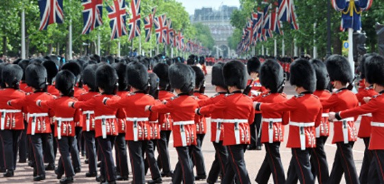 A wide shot of The Royal Guard marching under a row of British flags.