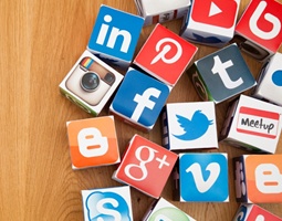 Many cardboard cubes grouped together on a wooden surface, each with a different social media platform logo printed onto it.