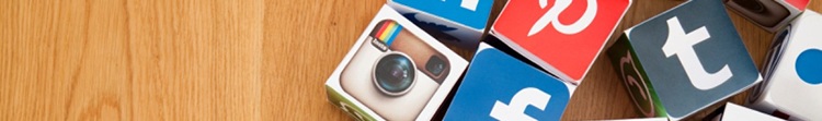 Many cardboard cubes grouped together on a wooden surface, each with a different social media platform logo printed onto it.