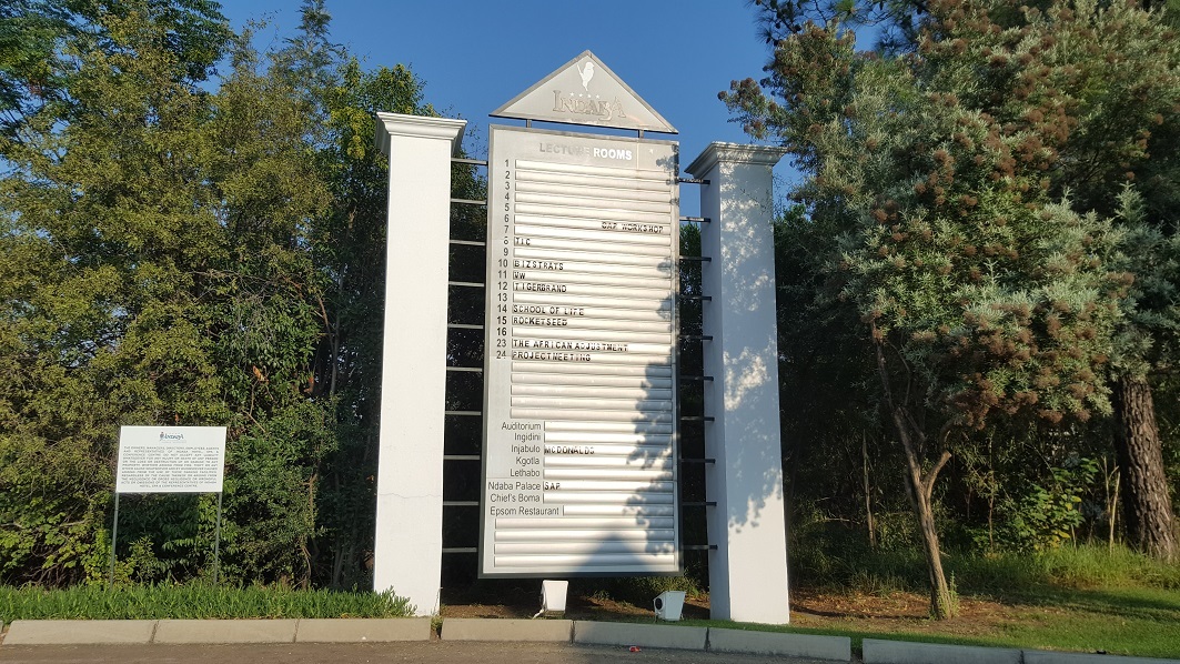 A tall notice board listing various lecture titles, surrounded by shrubs.