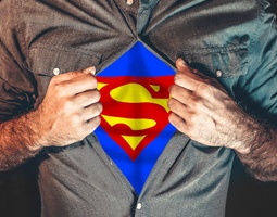 A torso shot of a man pulling open his shirt to reveal the Superman symbol.