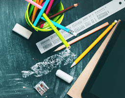 Pencils, a ruler, chalk and an eraser sit on a chalkboard background.