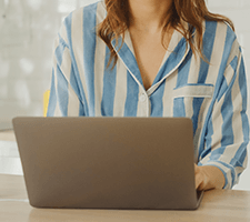 A woman sits behind a laptop in a striped blue shirt.