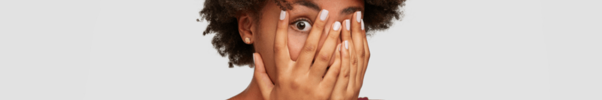 A close-up of a woman covering her face with her hands, with one eye visible.