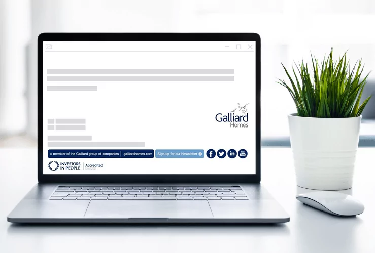 A laptop next to a potted plant, with the Galliard Homes email signature visible on screen.