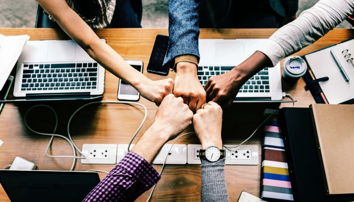 Five arms reach over laptops to fist bump in the center of a table.