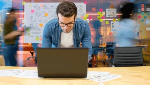 A man standing behind a laptop with a blurred office background
