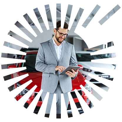 A guy standing in front of a red car in a dealership, working on his tablet